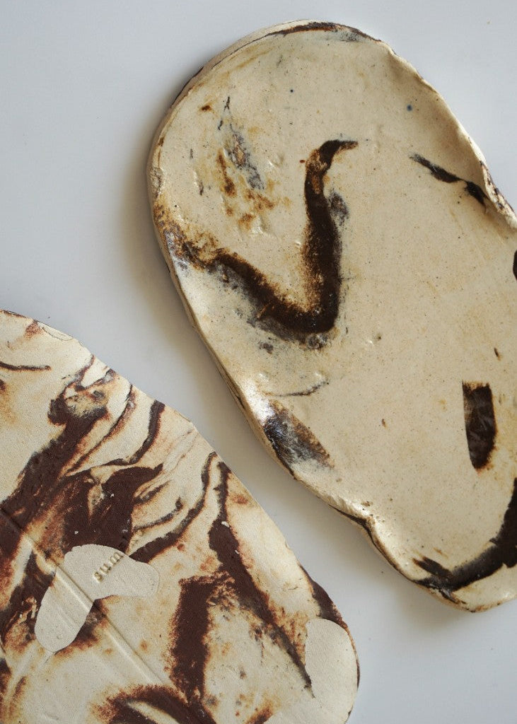 Two handmade ceramic coasters with a marbled pattern of cream, beige, and dark brown, displayed on a light gray background.