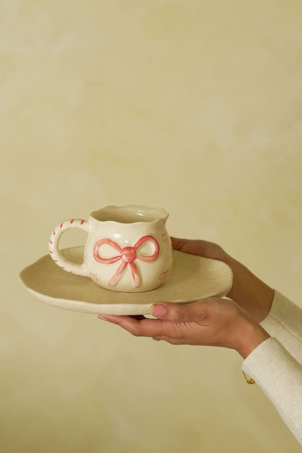 Ceramic pitcher with pink bow design held on a plate against a beige background