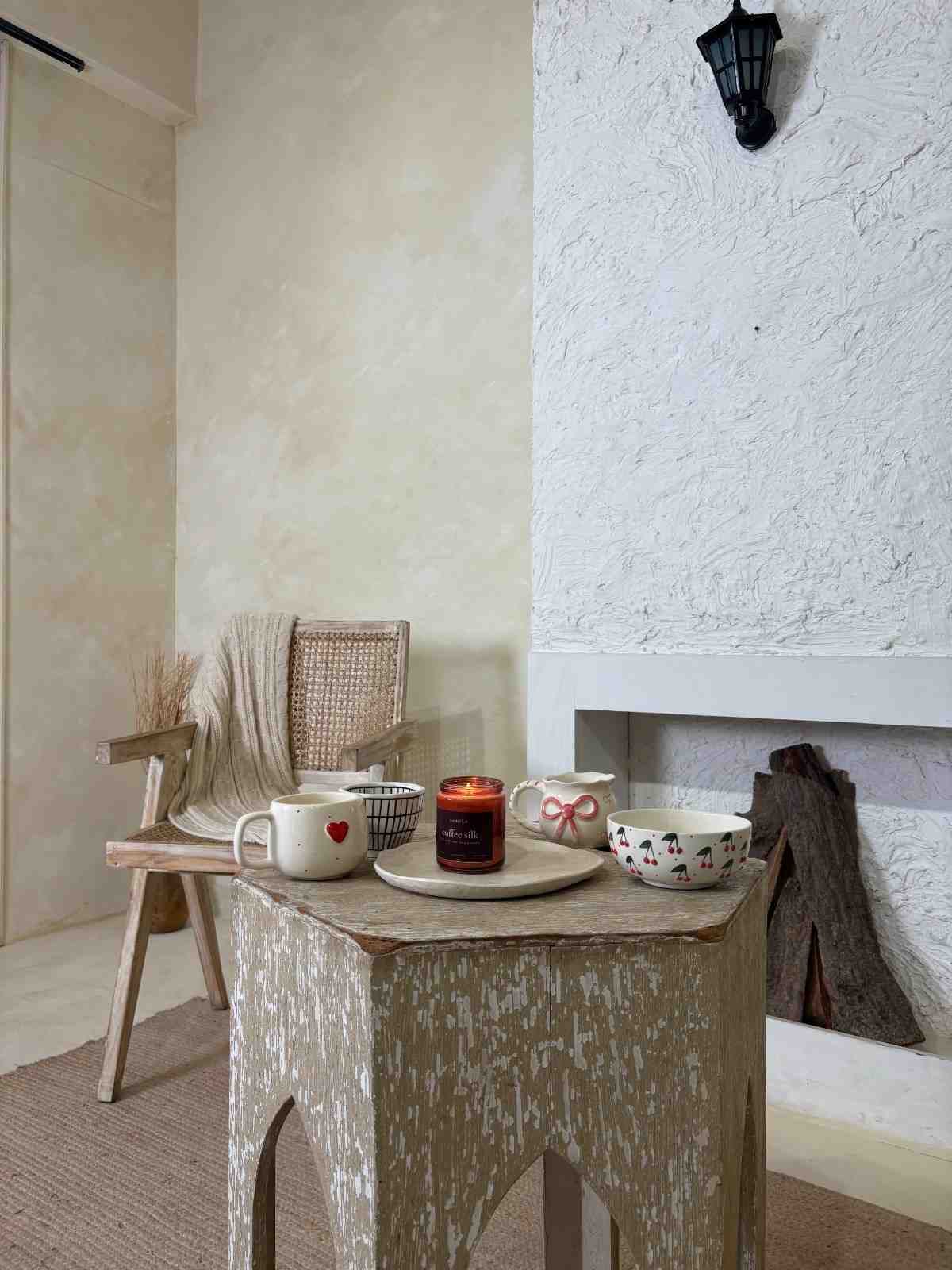 Small wooden table with a candle and cups in a cozy room.