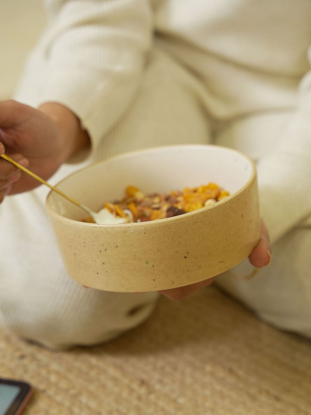 Person holding a bowl of cereal with a spoon, sitting on a couch.