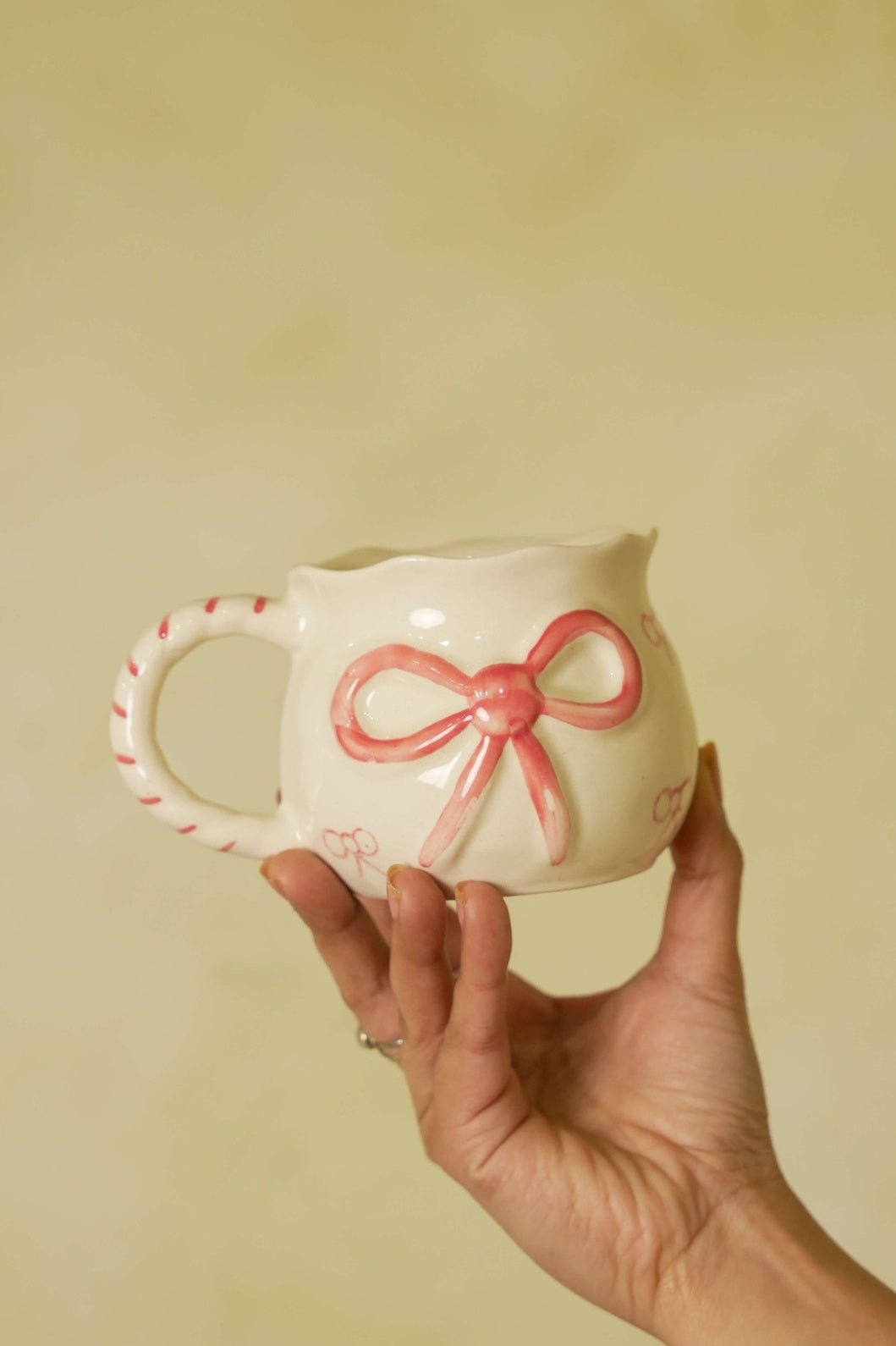 Ceramic mug with a pink bow design held by a hand against a beige background