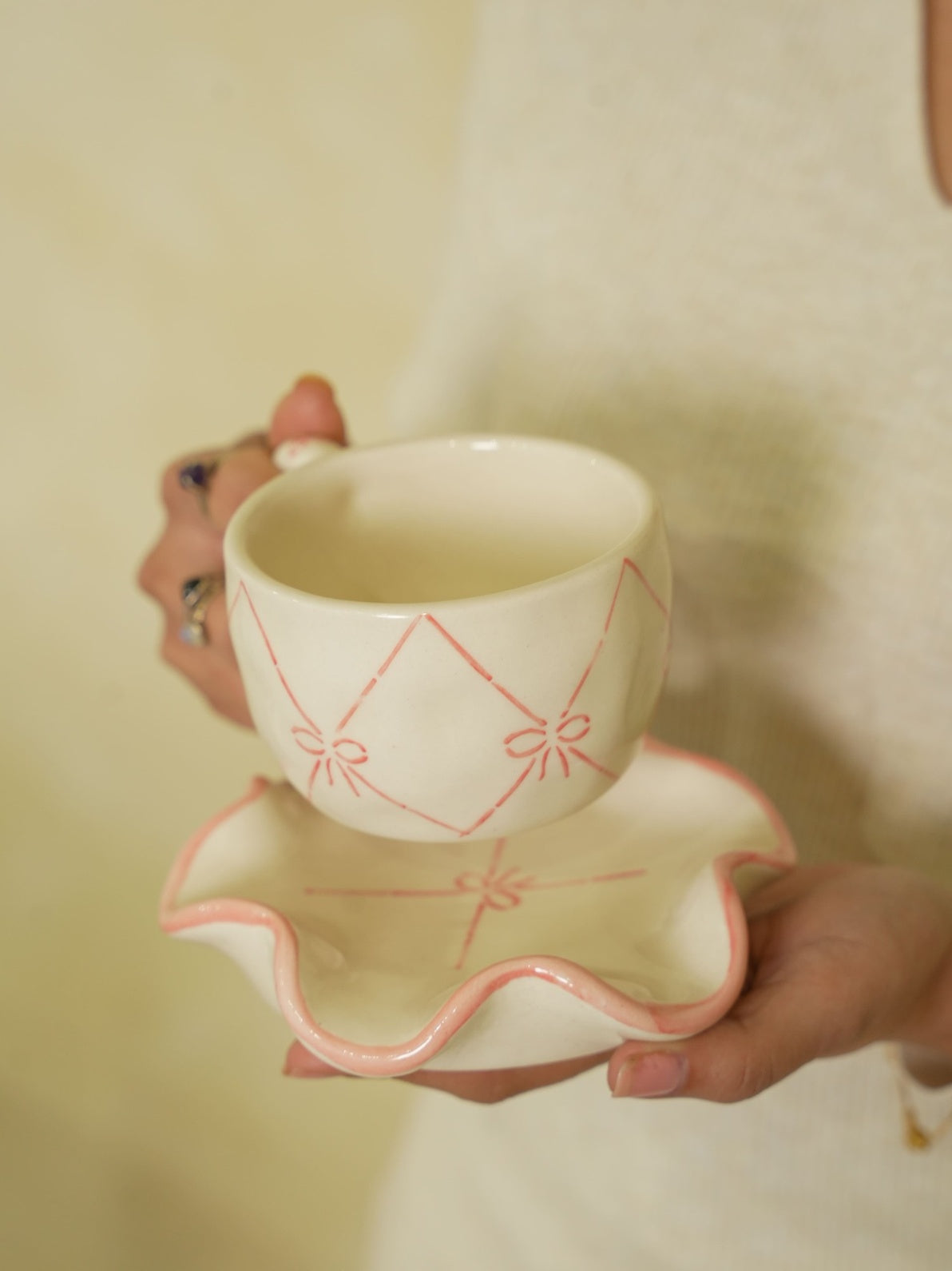 Ceramic cup with saucer held by a person against a plain background