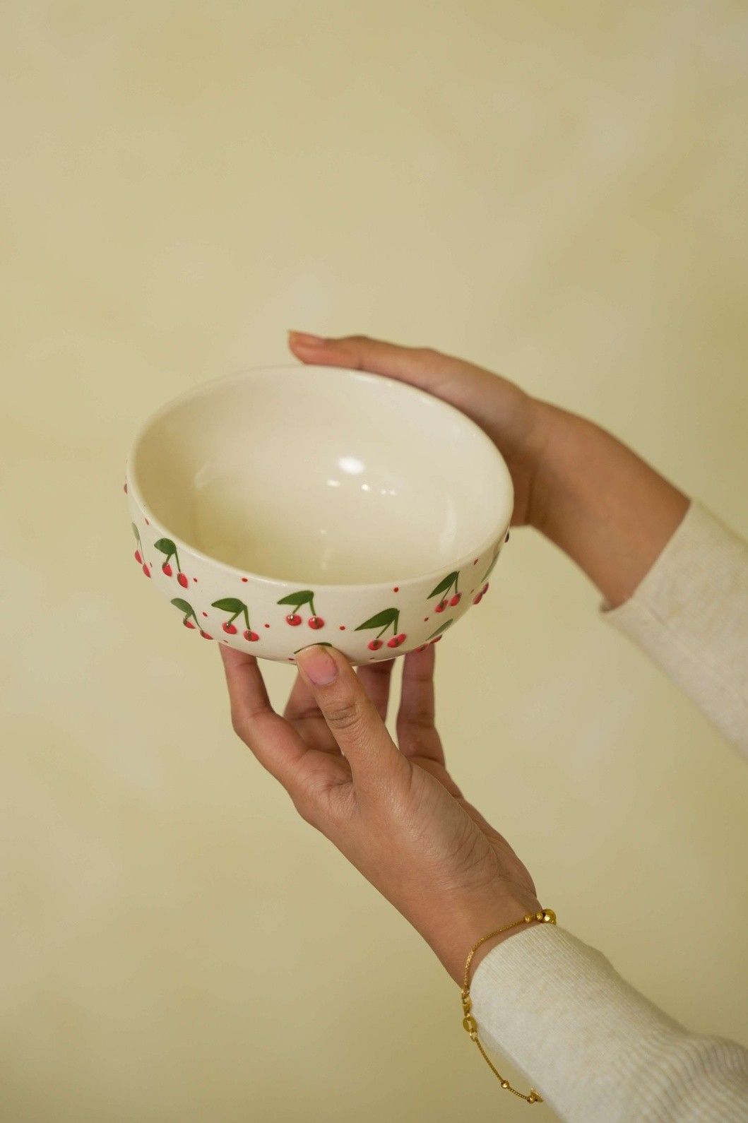 Hand holding a ceramic bowl with cherry design against a plain background