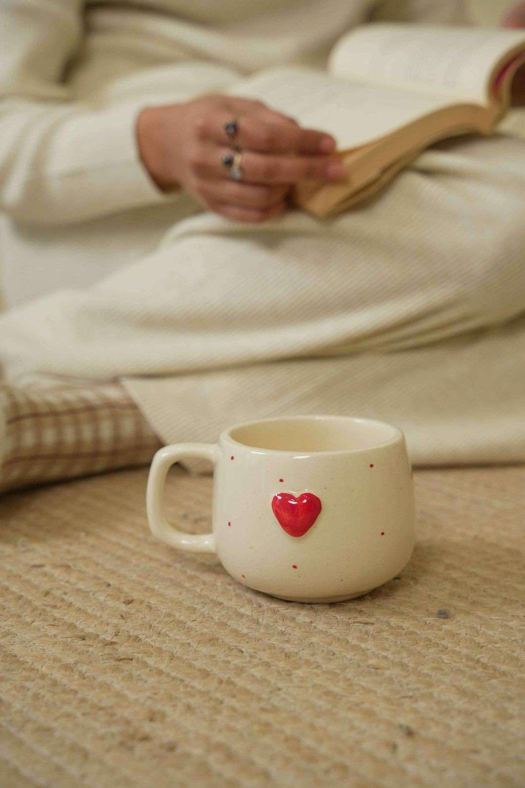 Sumeko Ceramic Heart mug with a red heart on a wooden surface, person holding a book in the background.