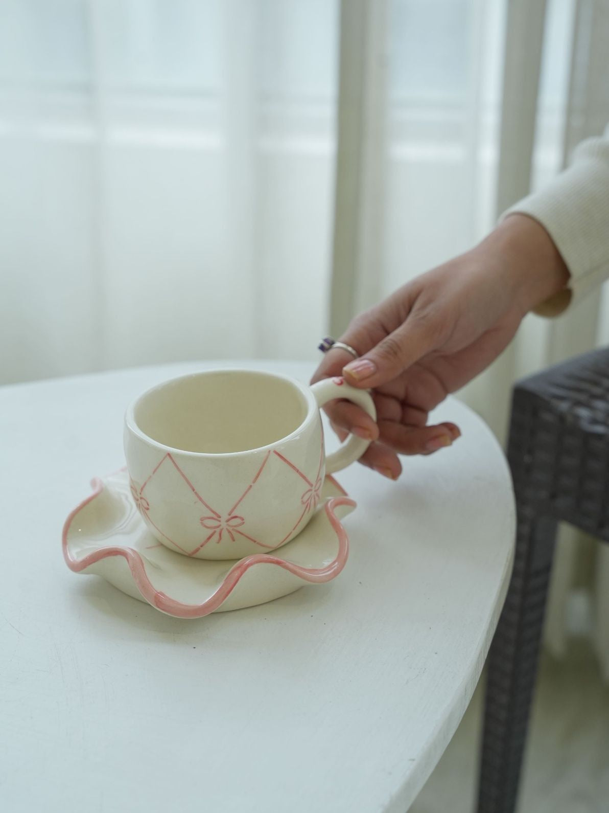 Person holding a ceramic cup with a matching saucer on a white surface.