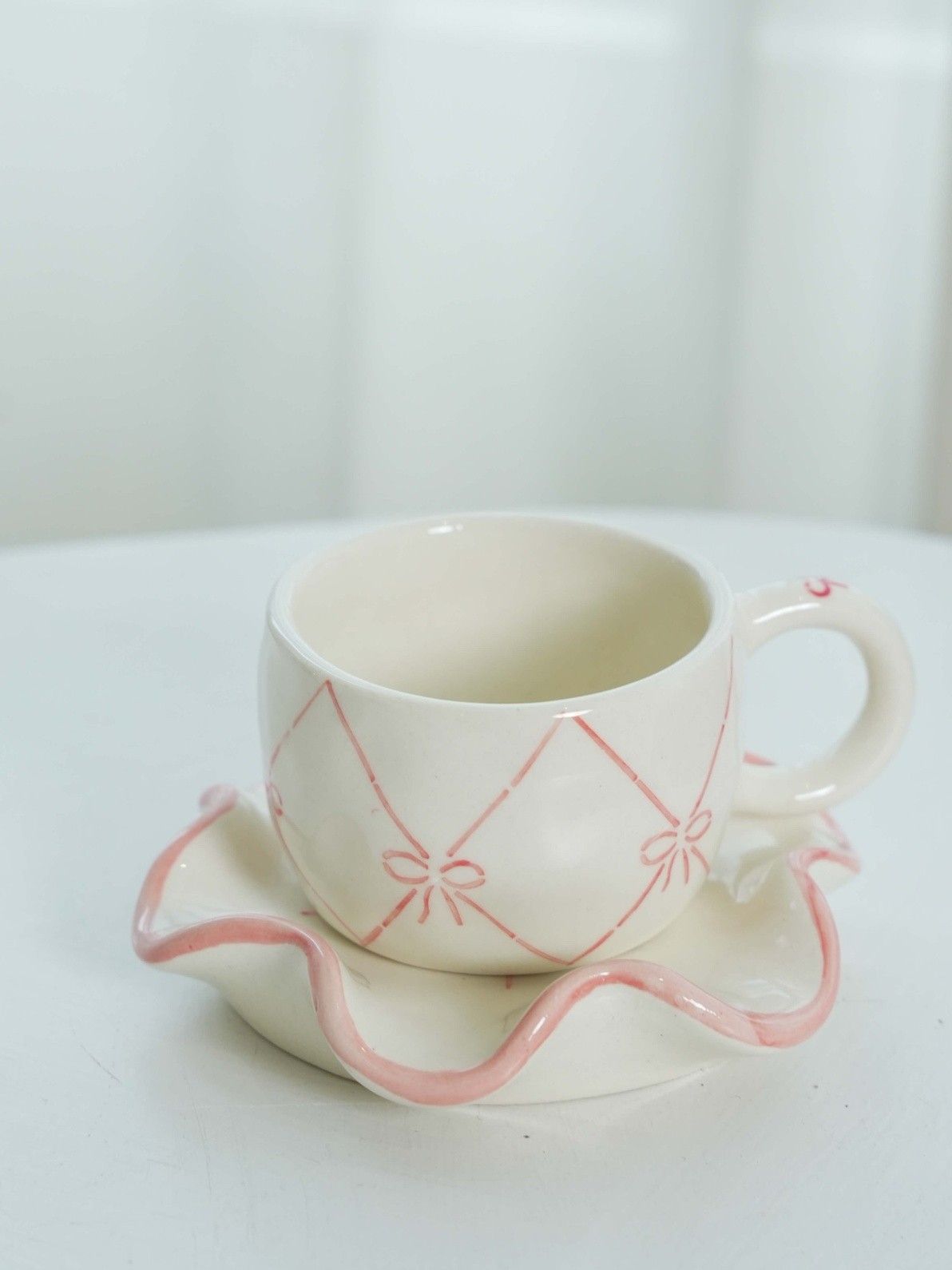 Ceramic cup with saucer featuring pink decorative elements on a white background