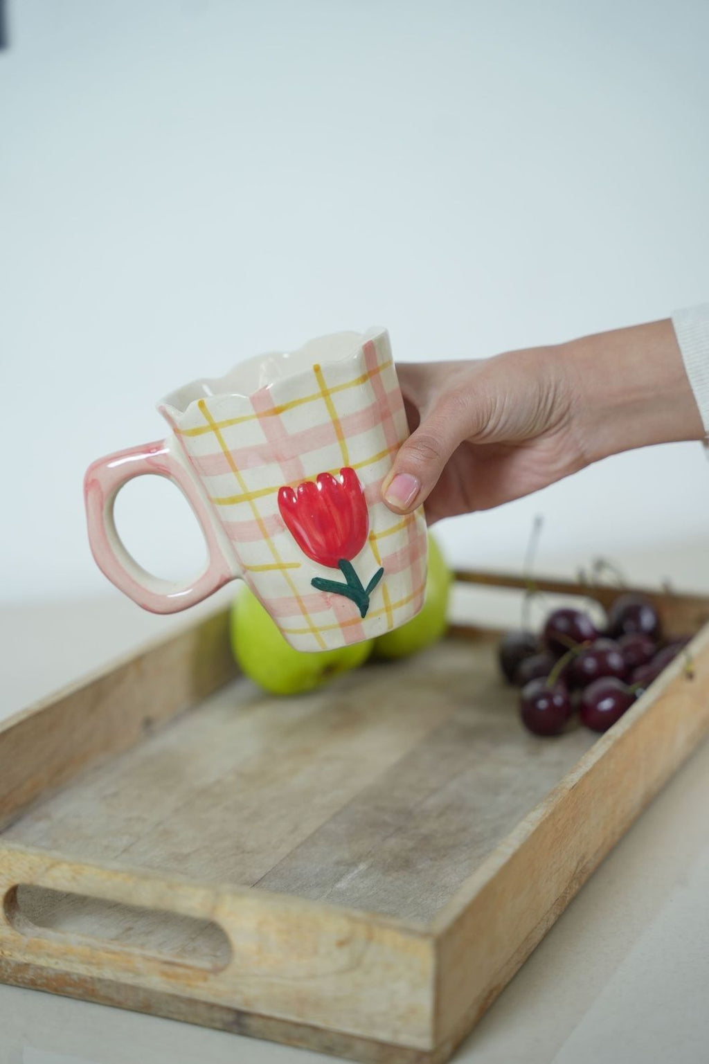 Hand holding a mug with a floral design on a wooden tray with fruits