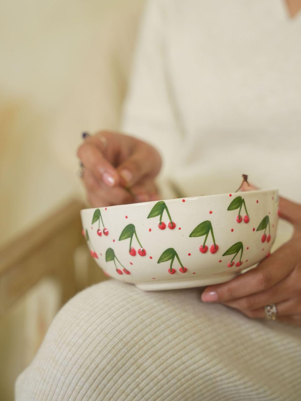 Person holding a bowl with cherry pattern on a neutral background