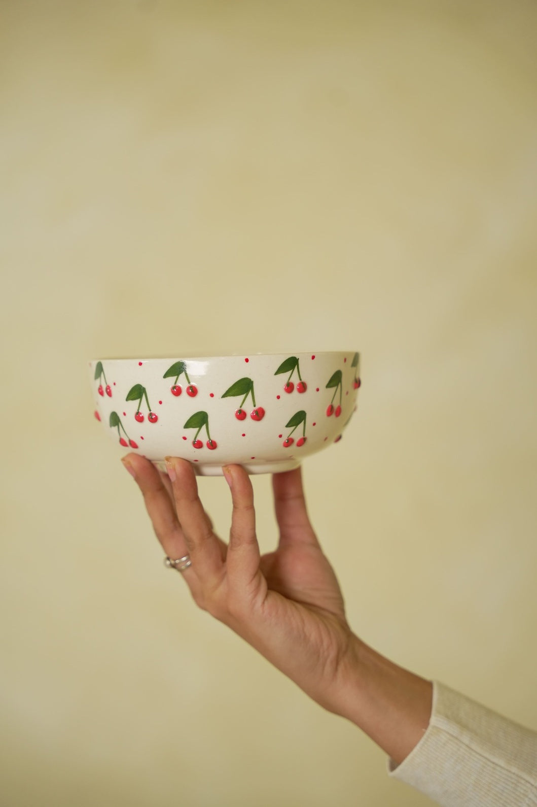 Hand holding a small bowl with cherry design against a plain background