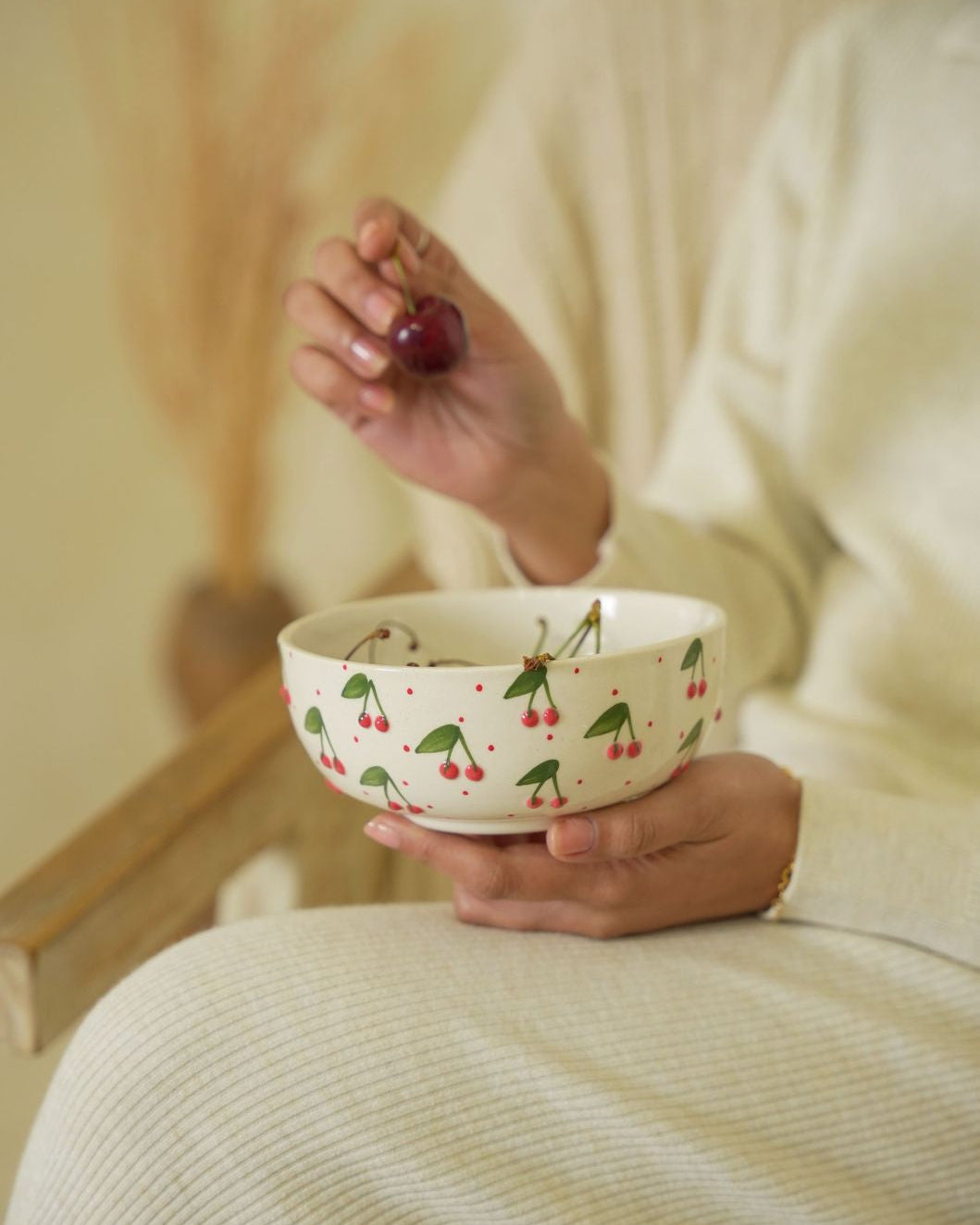 Person holding a bowl with cherry design and a cherry in their hand, sitting on a couch.