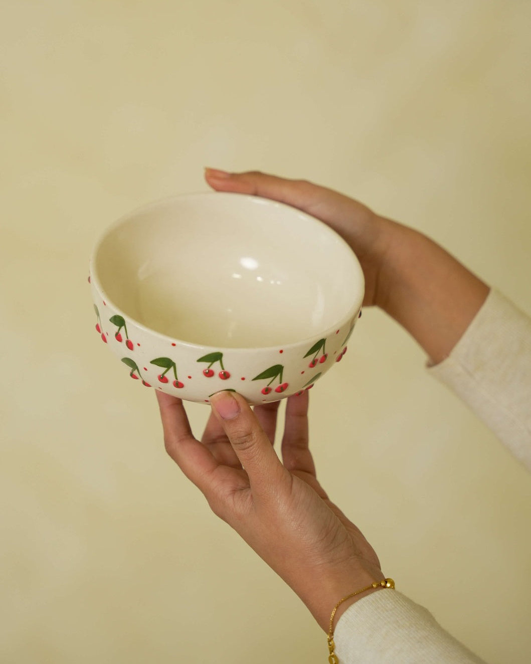 Hand holding a white bowl with cherry design against a beige background