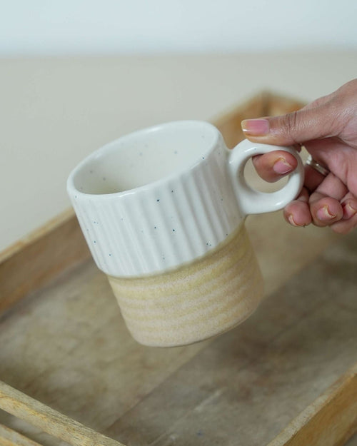Hand holding a ceramic mug with a textured design on a wooden surface.