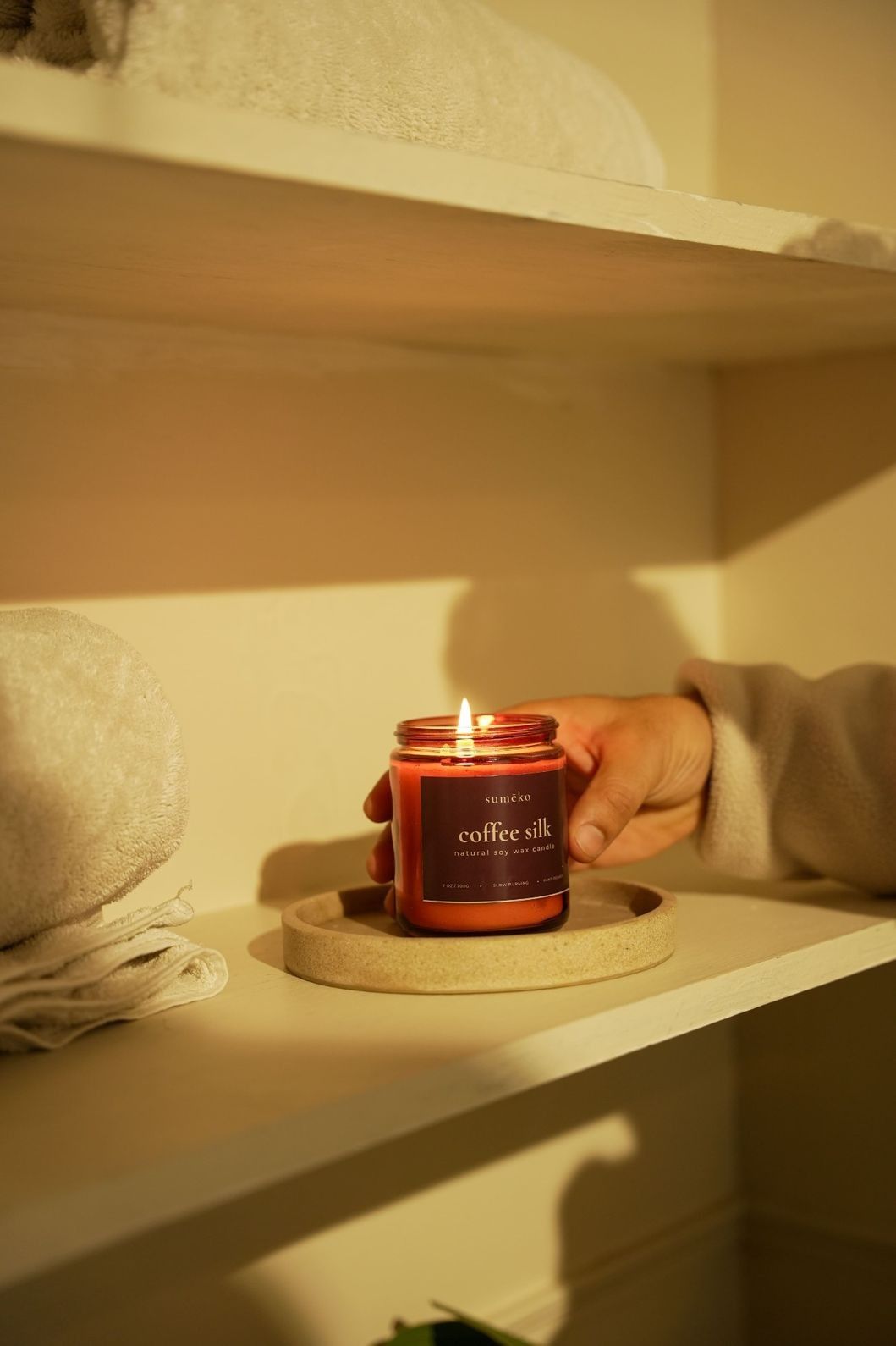 Hand holding a 'coffee silk' candle on a shelf with soft lighting