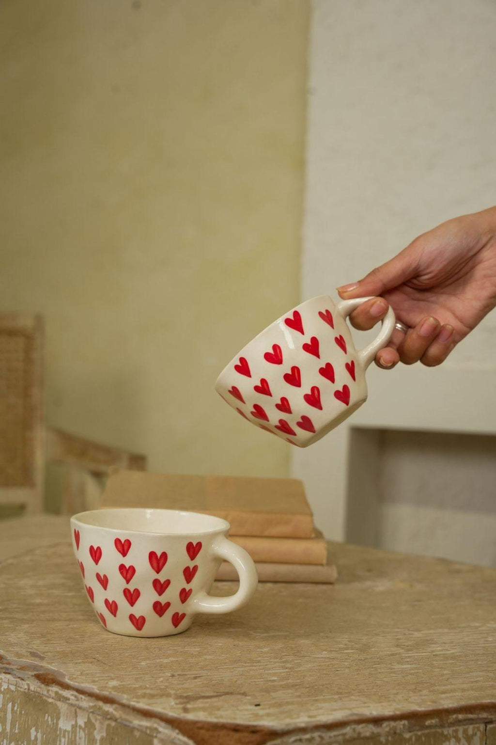 Person holding a mug with red heart pattern on a wooden surface