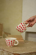 Person holding a mug with red heart pattern on a wooden surface