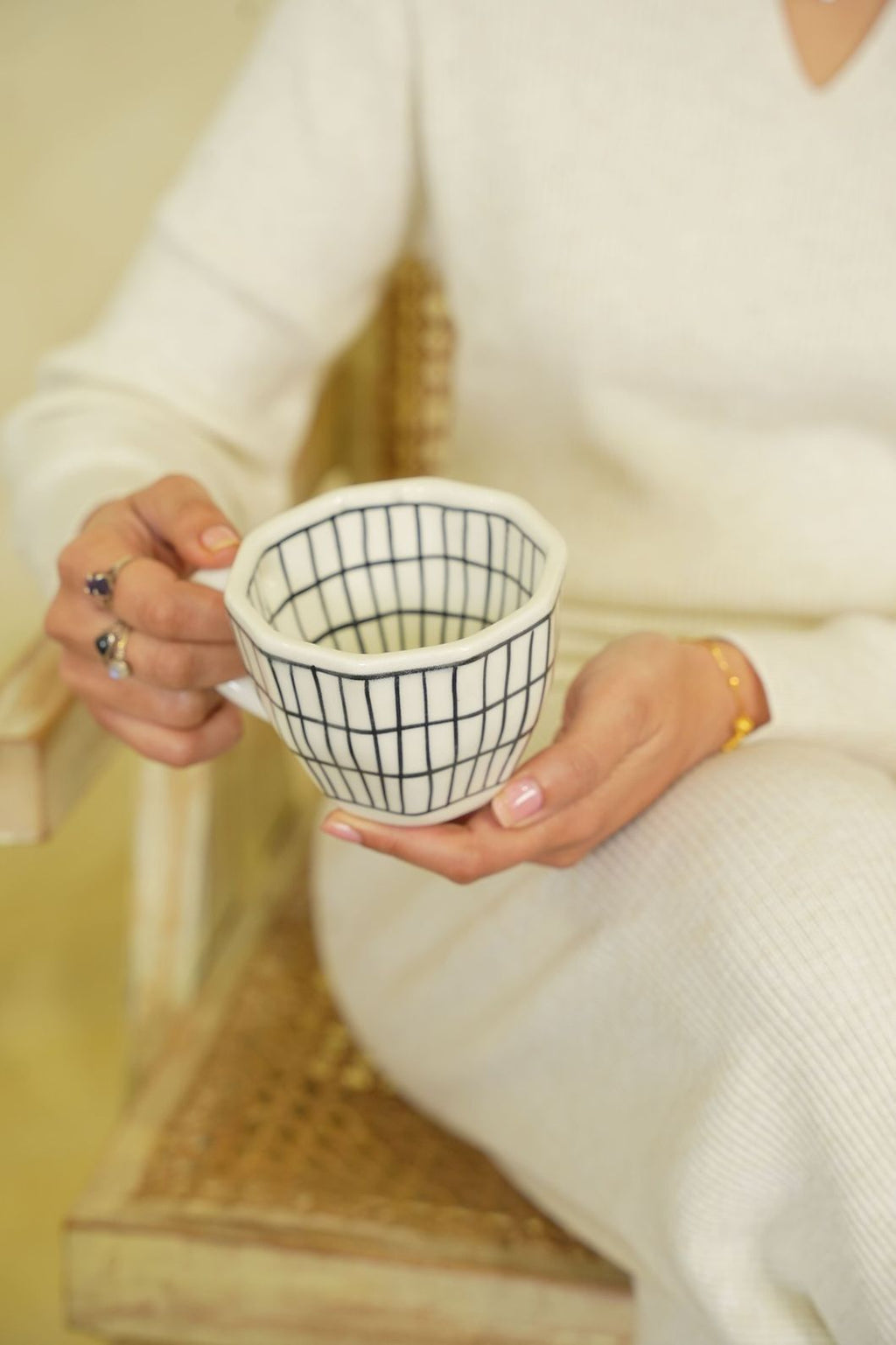 Person holding a white mug with black grid pattern, wearing a white sweater.