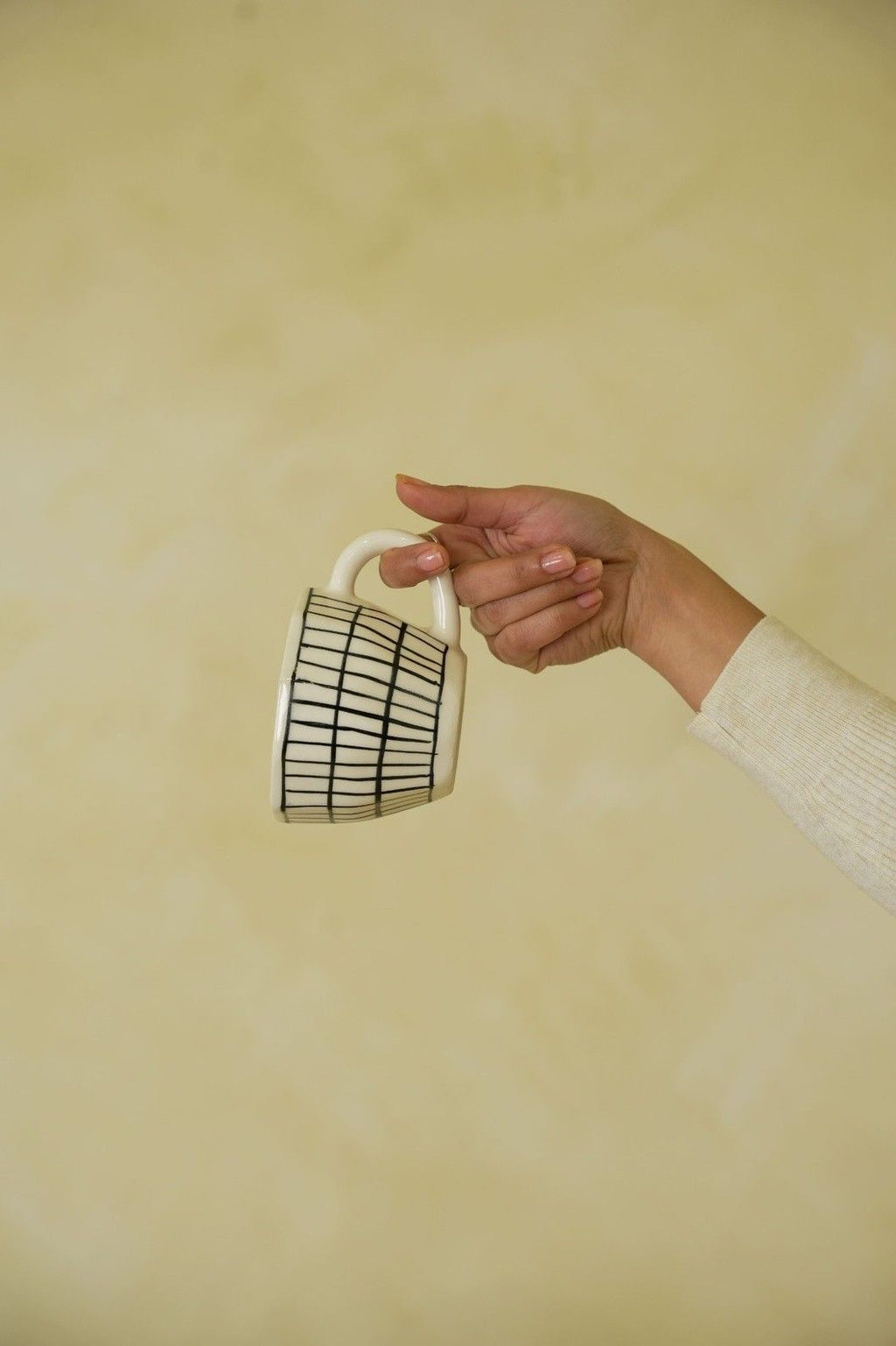 Hand holding a white mug with black grid pattern against a beige background