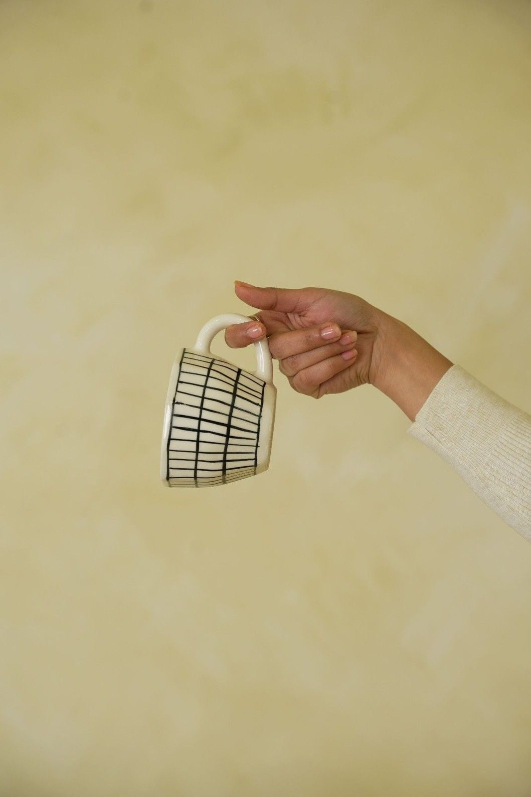 Hand holding a white mug with black grid pattern against a beige background