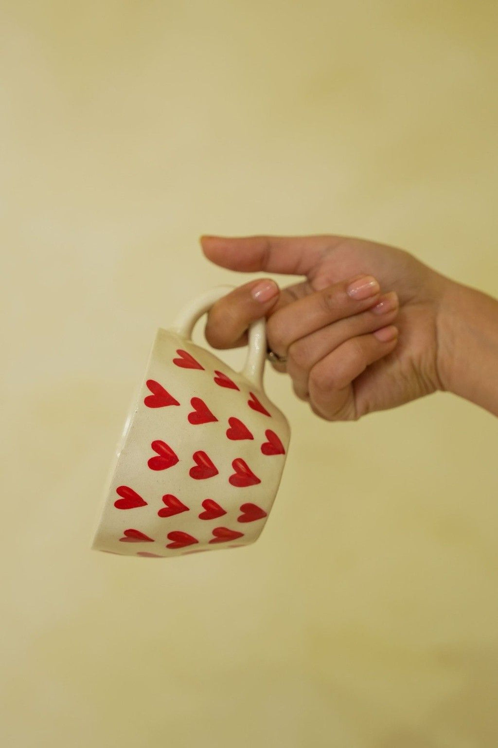 Hand holding a small white bag with red heart patterns against a plain background
