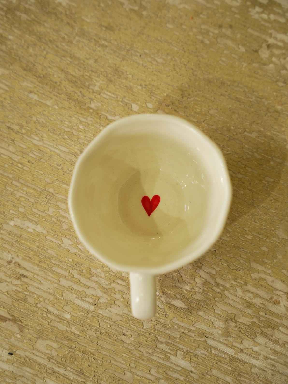 White ceramic cup with a red heart on a wooden surface
