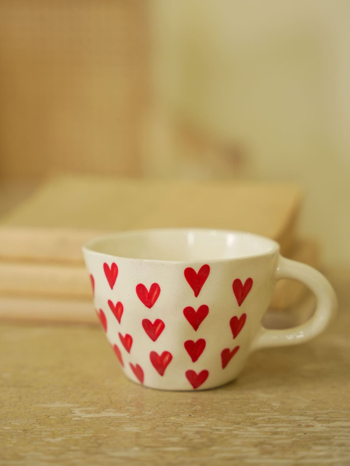 Ceramic mug with red heart patterns on a wooden surface.