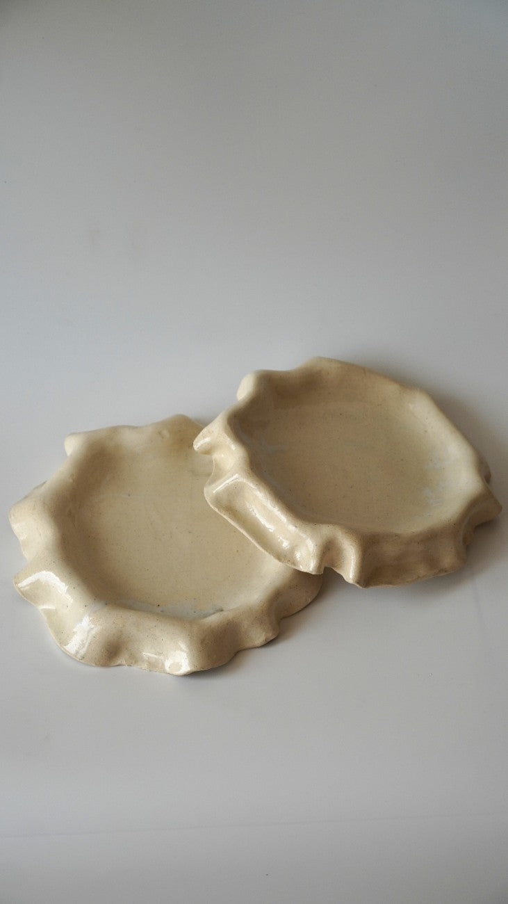 Two small, organic-shaped ceramic dishes with a ruffled edge and a glossy cream glaze, displayed on a light gray background.