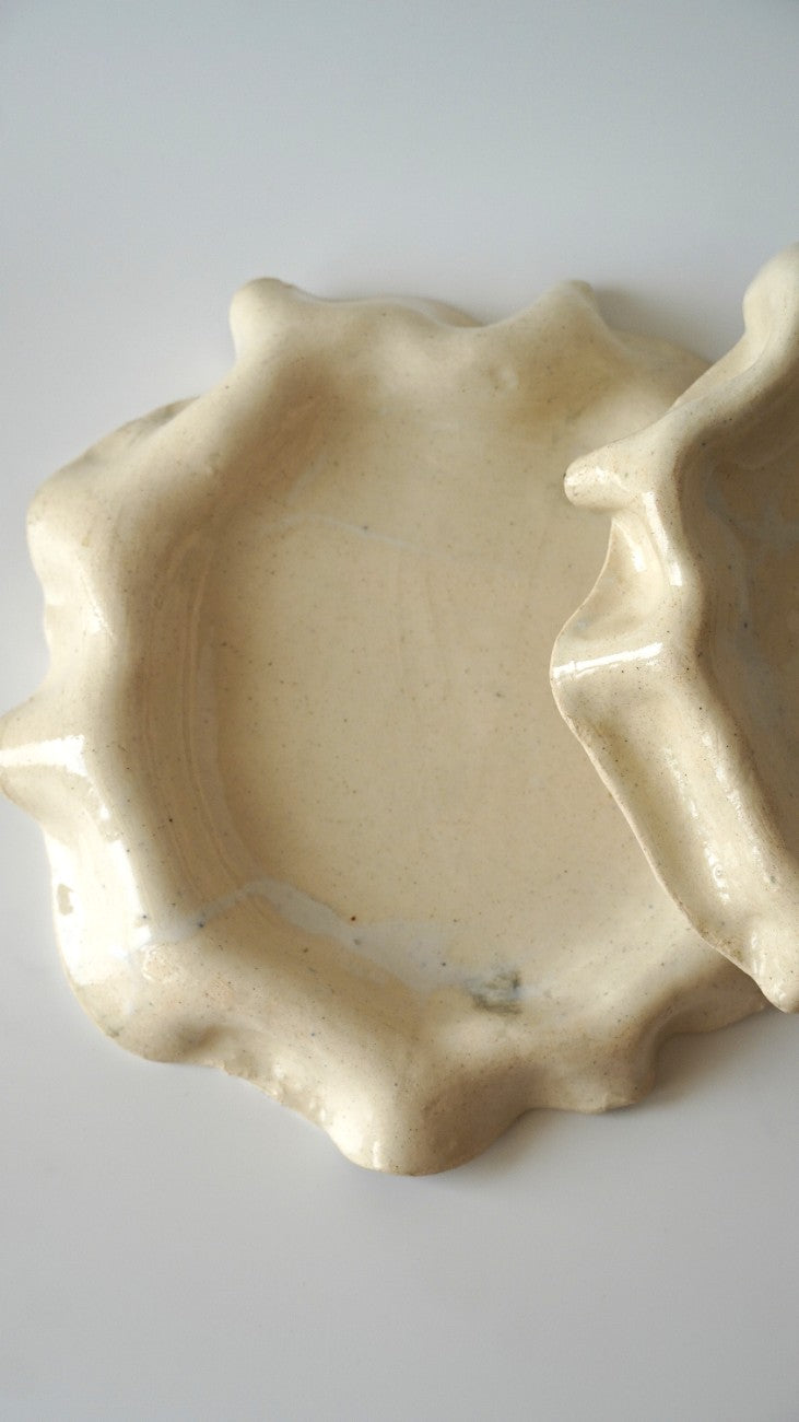 A handmade ceramic dish with a wavy, organic scalloped rim and a glossy finish, shown on a plain light gray background.