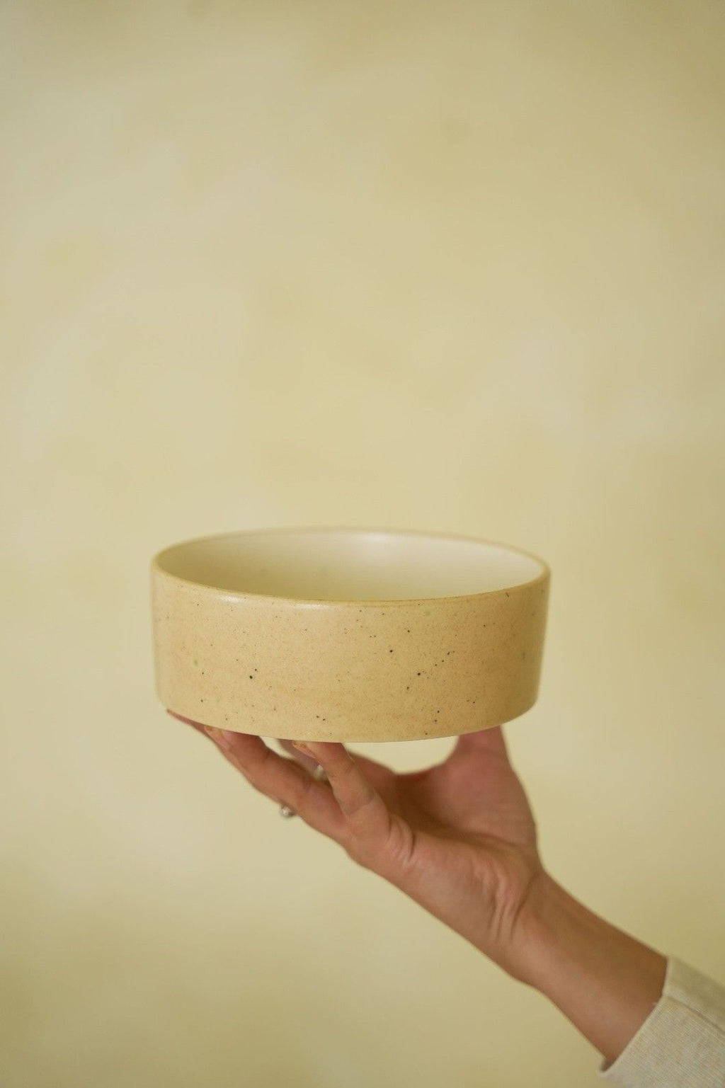 Hand holding a beige ceramic bowl against a plain background