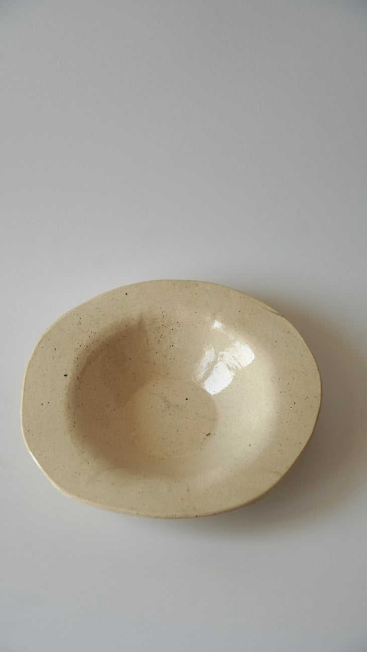 A small, shallow, oval ceramic dish with a speckled cream-beige glaze, photographed from directly above on a neutral light gray background.