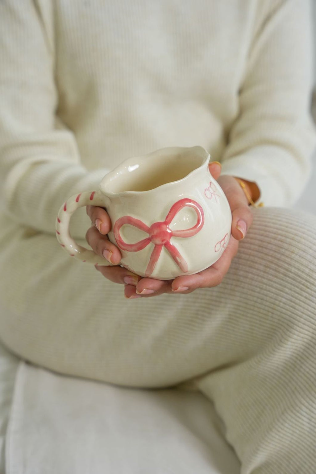 Person holding a ceramic mug with a pink bow design against a neutral background