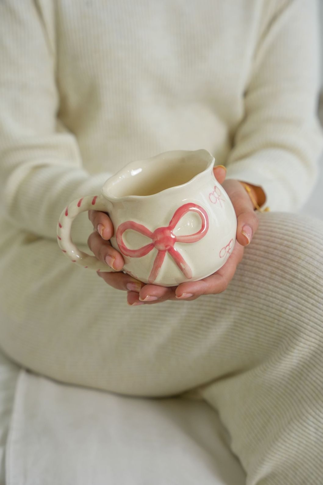Person holding a ceramic mug with a pink bow design against a neutral background