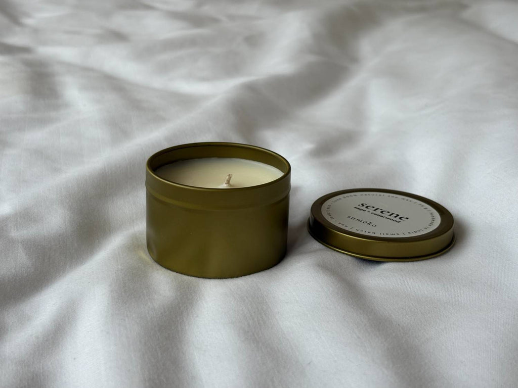 Scented candle in a metal tin with lid on a white fabric background