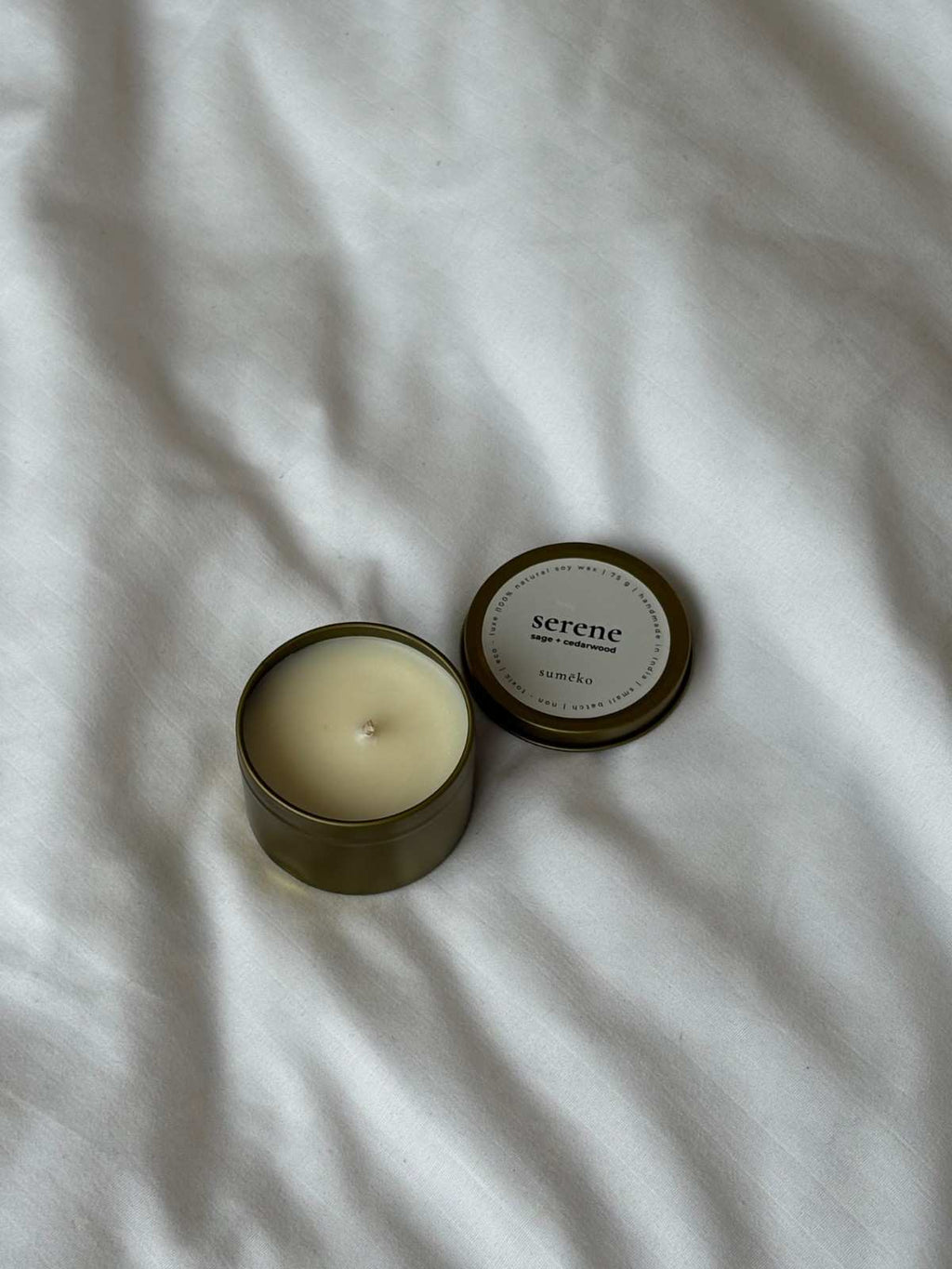 Scented candle in a tin with lid on a white fabric background