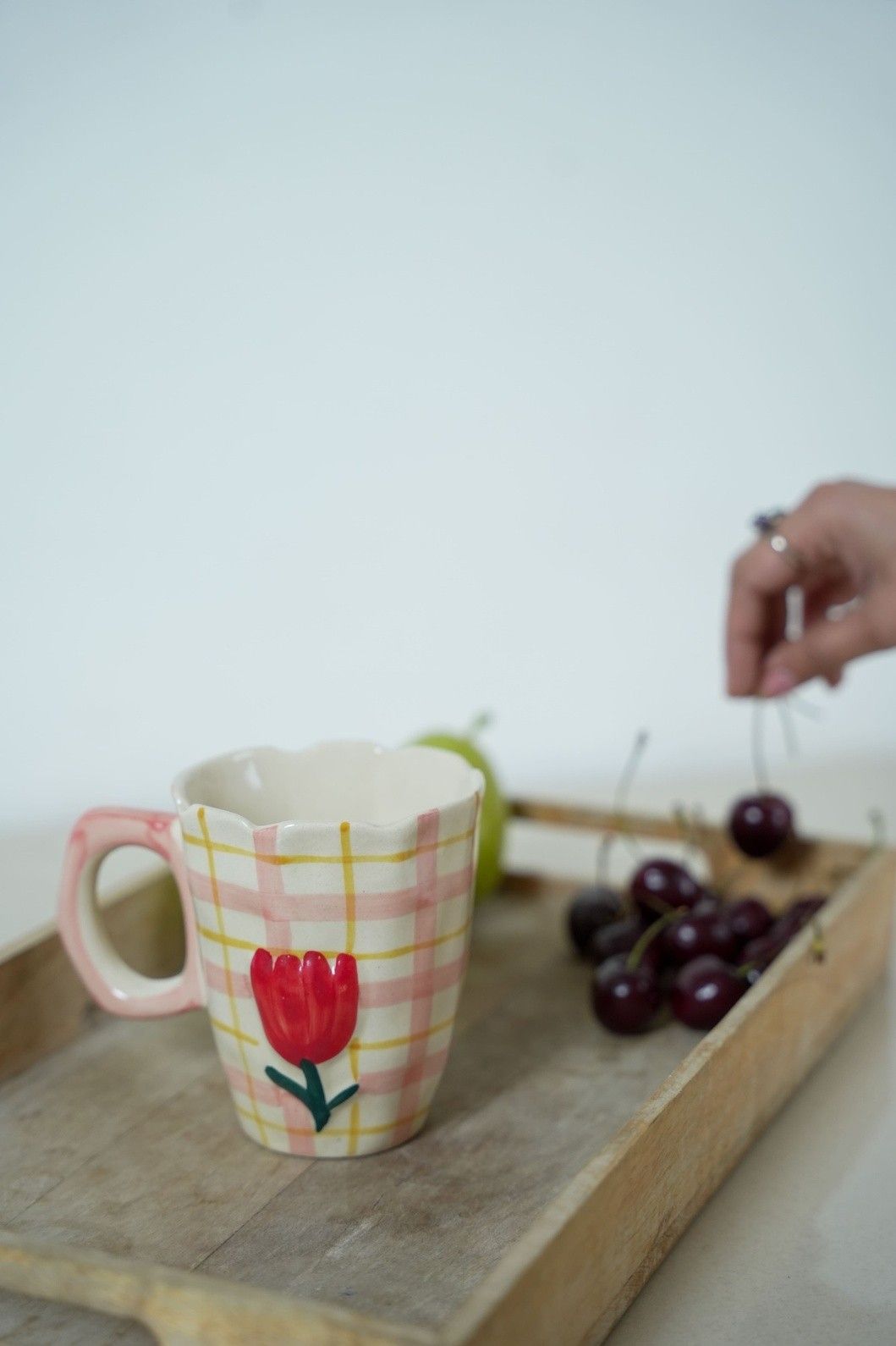 Ceramic mug with a red tulip design on a wooden tray with grapes