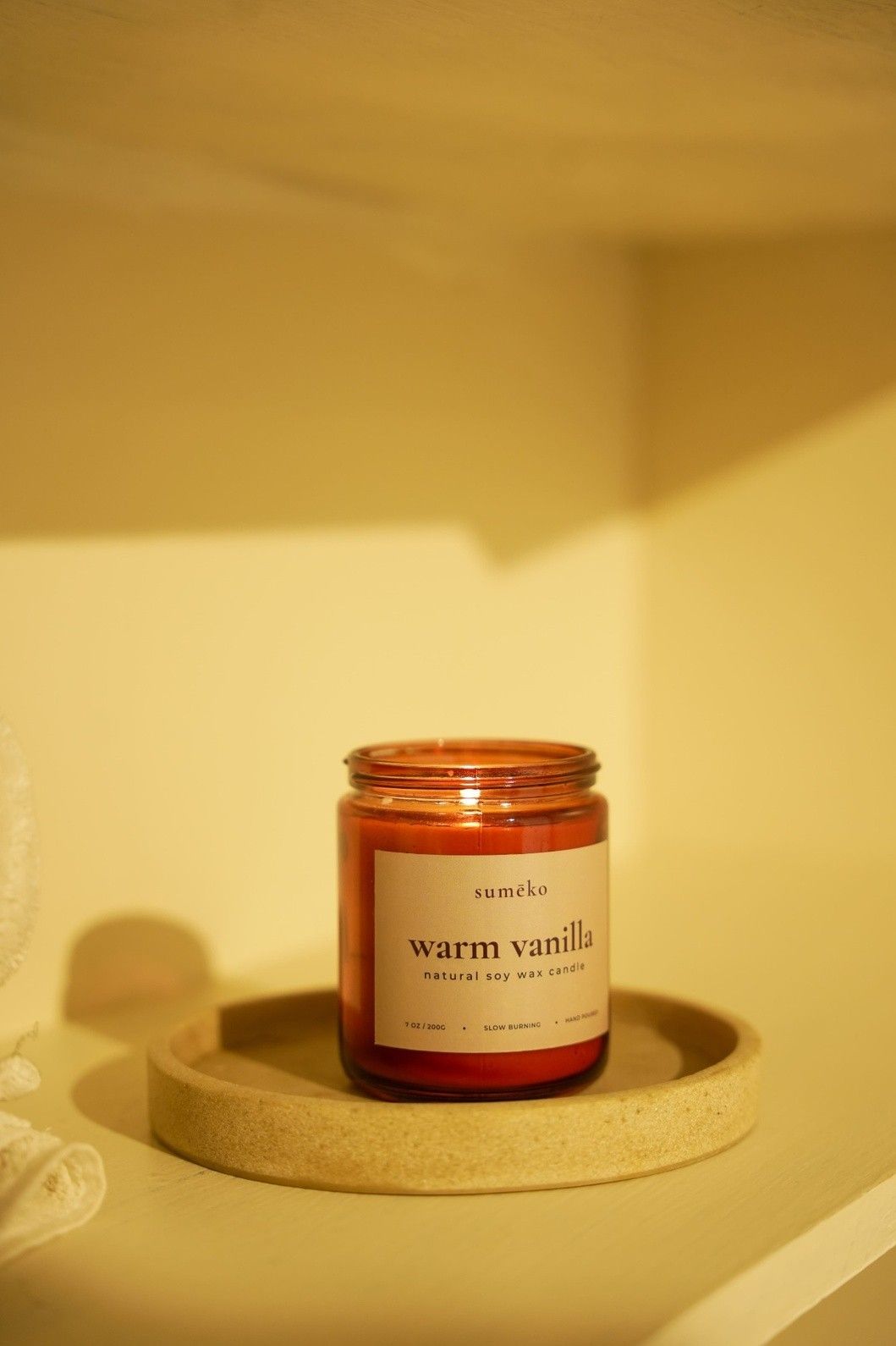 Candle labeled 'warm vanilla' on a textured surface with a warm glow